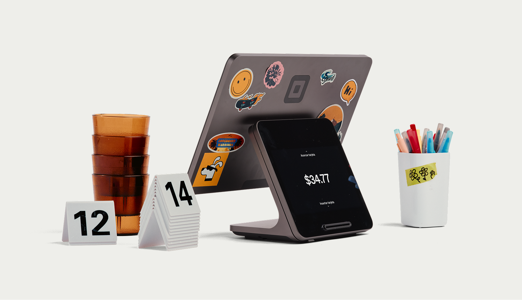 Square Register in studio with stickered merchant screen, customer display, amber cups, table numbers, and pen cup — Here for the Good Stuff
