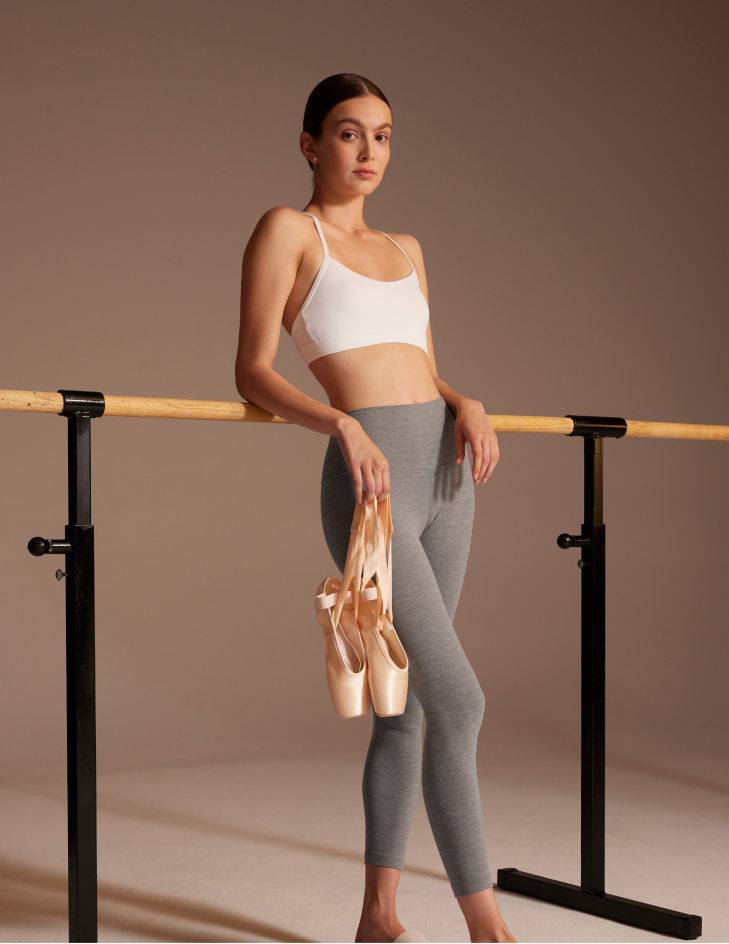 lululemon studio — model at ballet barre in grey leggings and white sports bra, holding pointe shoes, neutral backdrop